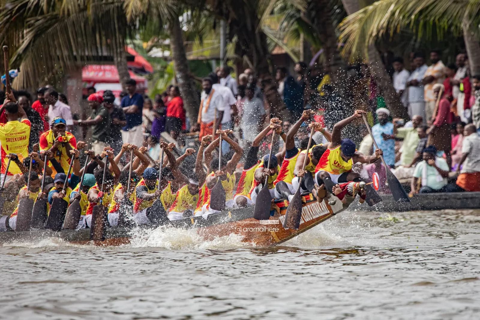 VBC Kainakary crew mid-stroke as spectators line the bank