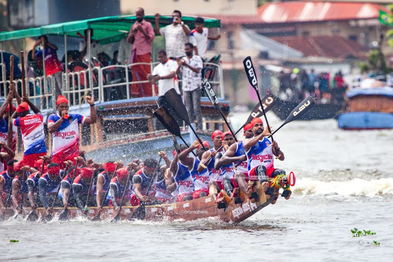 Crew in red and blue raising their paddles as the boat surges ahead